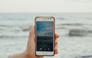 A hand holding a phone in front of an ocean