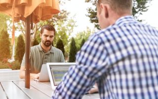 Two men sit away from each other on laptops